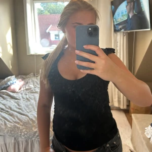 Svart topp med volang från Bik Bok - Svart ärmlös topp från Bik Bok med volangdetaljer vid axlarna och längs den djupa rundade urringningen. Den är storlek L men passar mig som oftast har S/M. Den är stretchig