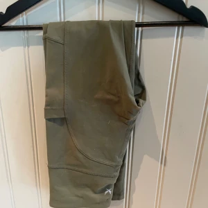 Olivgröna leggings från SOC XS - Snygga olivgröna leggings från SOC i storlek XS. De är tillverkade i ett stretchigt syntetmaterial med teknisk TCS Airflow-funktion som håller dig torr och bekväm. Perfekta för träning eller chill dagar. Snygga sömdetaljer och diskret logga vid benet.