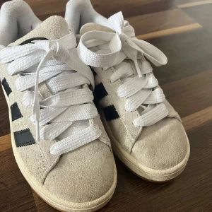 Adidas Campus sneakers beige mocka - Säljer ett par Adidas Campus sneakers i beige mocka med svarta ränder och vit sula. Skorna har klassisk rund tå, platt gummisula och kommer med både vita och svarta skosnören. Perfekta för dig som gillar retrostil och streetwear.