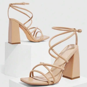 Beige sandaler med blockklack - Snygga beige sandaler med höga blockklackar och smala remmar som slingrar sig runt foten och ankeln. Sandalerna har öppen tå och fyrkantig sula, vilket ger en modern vibe. Perfekta för dig som gillar stilrena och trendiga skor med extra höjd.