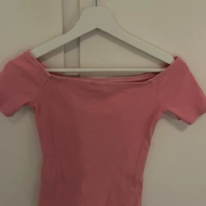 Rosa offshoulder topp från Nelly - Supersöt rosa offshoulder topp från Nelly i ribbad bomull. Tight passform och korta ärmar, perfekt för dig som vill ha en enkel men trendig look. Passar till både jeans och kjol för en chill vibe.