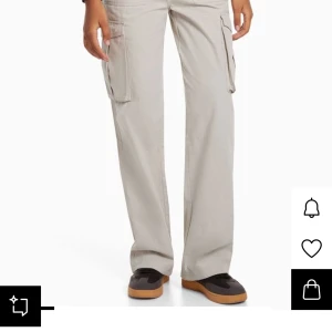 Beige cargo pants från Bershka - Snygga beige cargobyxor från Bershka med raka ben och flera stora fickor på sidorna. Byxorna har normal passform och är tillverkade i bomull, perfekta för en avslappnad streetstil. Klassisk midja och praktiska detaljer gör dem till ett måste i garderoben.