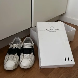 Valentino Garavani Open sneakers vit/svart - Skriv till mig om ni vill köpa de och vi kan snacka om priset om ni vill ha det billigare. Snygga Valentino Garavani Open sneakers i vitt skinn med bred svart rem över vristen. Klassisk rund tå, vita snören och platt sula. Kommer med originalkartong och dustbag. Perfekta för dig som gillar exklusiva och stilrena sneakers.