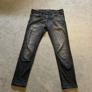 Svarta slim jeans Jack & Jones 31/32 - Svarta slim fit jeans från Jack & Jones, modell Glenn. Jeansen har klassisk femficksdesign, dragkedjegylf och snyggt tvättad finish. Materialet är stretchigt för extra komfort och passformen är smal hela vägen ner.