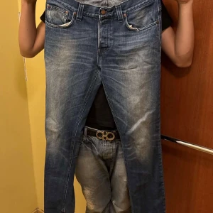 Nude jeans - Säljer ett par klassiska blå jeans med snygga slitningar och tvättade detaljer. Jeansen har raka ben, fem fickor och normal passform. Perfekta för dig som gillar en avslappnad och tidlös look.