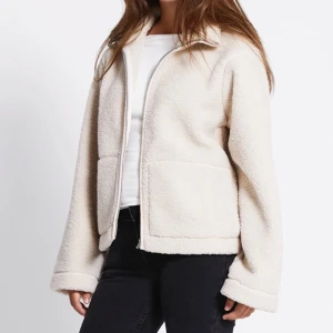 Beige teddyjacka med dragkedja - Mysig beige teddyjacka med stora fickor framtill och dragkedja. Jackan har en avslappnad passform och är tillverkad i fluffigt teddy-material som håller dig varm. Perfekt för lager-på-lager och chill höst- eller vinterstil.