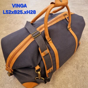 Blå weekendbag från Vinga med detaljer i skinn - Snygg och rymlig weekendbag från Vinga i mörkblått tyg med bruna skinnhandtag och detaljer. Väskan har justerbar axelrem, dragkedja upptill och mäter ca 52x25x28 cm. Tillverkad i återvunnen polyester med klassisk look och rutigt innerfoder.