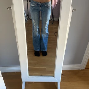 Blå bootcut jeans från Gina Tricot - Säljer ett par ljusblå bootcut jeans från Gina Tricot i storlek 152. Jeansen har rosa kontrastsömmar, broderade bakfickor med knapp och klassisk femficksdesign. Materialet är jeans och passformen är relaxed med utsvängda ben. använda en gång