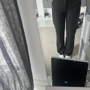 Svarta randiga kostymbyxor Kappahl - Svarta kostymbyxor från Kappahl med vita tunna ränder. Byxorna har normal passform, raka ben och klassisk midja. Snyggt skräddad look med fickor bak och knappstängning fram. Passar inte mig längre. 