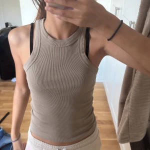 Beige ribbad linnetopp från Gina Tricot - Säljer en beige ribbad linnetopp från Gina Tricot, basically basics-kollektionen. Toppen är ärmlös med rund halsringning och har en tight passform. Perfekt att styla med jeans eller shorts för en chill look.