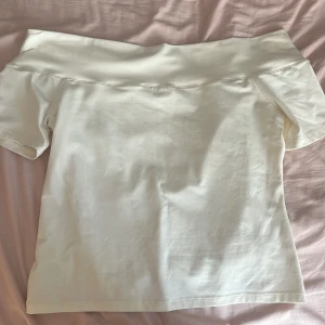 offshoulder topp - Säljer en stilren vit/gräddvit offshoulder topp med korta ärmar. Toppen har en bred kant upptill som ger en snygg och modern look. Perfekt för dig som gillar minimalistisk stil och vill ha något enkelt men ändå trendigt. Gjord i mjuk bomull för skön känsla. Denna är perfekt nu till hösten 
