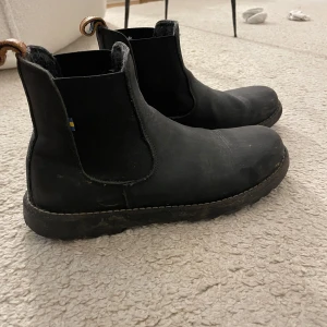 Svarta chelsea boots från Kavat - Stilrena svarta chelsea boots från Kavat i skinn med klassisk rund tå och elastiska sidor. Snygga detaljer med bruna dragflikar bak och grov sula. Perfekta för höst och vinter när du vill ha både stil och funktion.