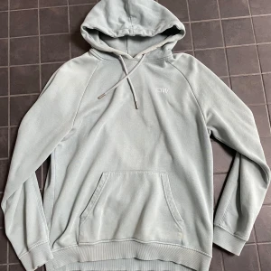 Ljusblå hoodie från ICANIWILL - Säljer en stilren ljusblå hoodie från ICANIWILL med broderad logga på bröstet. Tröjan har huva med snörning, känguruficka och ribbade muddar. Hoodien är inte i nyskick och färgen är något sliten!