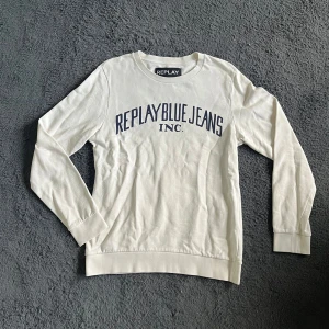 Replay tröja  - Vit långärmad tröja från Replay med blå text 'REPLAY BLUE JEANS INC.' framtill. Tröjan har rund halsringning och är gjord i mjuk bomull. Perfekt för en avslappnad och stilren look. SKICKAR EJ BILD NÄR JAG BÄR DEN !