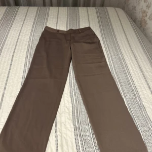 Bruna kostymbyxor från La Mode - Snygga bruna kostymbyxor från La Mode i storlek 46 men litet i modell. Passar dig som har 42/44Byxorna har raka ben, bälteshällor och är tillverkade i en mjuk mix av polyamid, bomull och elastan för en skön passform. Perfekta för dig som gillar en klassisk och stilren look. 