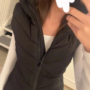 Svart dunväst från Zara med huva - Snygg svart dunväst från Zara med quiltad design och huva. Västen har dragkedja framtill och en figurnära passform. Perfekt att slänga över en hoodie eller långärmad tröja. Materialet är syntet och västen är lätt vadderad. Hör av dig vid minsta fråga!❤️