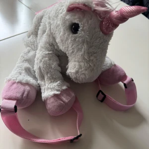 Unicorn ryggsäck i plysch med vingar - Supergullig ryggsäck formad som en enhörning i mjuk plysch. Väskan är vit med rosa detaljer, glittriga vingar och horn samt fluffig rosa svans. Justerbara axelband och dragkedja på ryggen. Perfekt för dig som vill sticka ut med en unik accessoar! Finns ej att finna i butik! Denna är rätt stor/rejäl jämfört med dom som finns på marknaden idag!