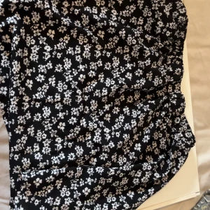 Svartvit blommig kjol från SHEIN - Supersöt svart kortkjol från SHEIN med vitt blommönster. Kjolen har en bekväm resår i midjan och är perfekt för dig som gillar en trendig och lekfull stil. Lätt och luftig, passar perfekt till sneakers eller sandaler.