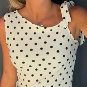Prickig topp - Supersöt vit klänning med svarta prickar och knyt på ena axeln. Ärmlös modell med rund halsringning, perfekt för varma dagar. Lätt och luftig känsla, passar dig som gillar en lekfull och trendig stil. L men partar M. Använd en gång!