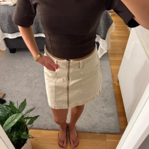 Beige jeanskjol från Gina tricot - Snygg beige kort jeanskjol från Gina tricot. Kjolen har en stilren, enkel design och ger en cool look.