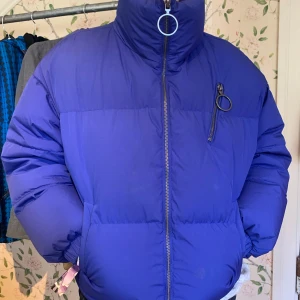 Blå pufferjacka från Benetton XS - Snygg blå dunjacka från United Colors of Benetton i storlek XS. Jackan har hög krage, stora ringar på dragkedjorna och en oversized look. Känns som att ha på sig ett täcke:) säljer pga brist på plats