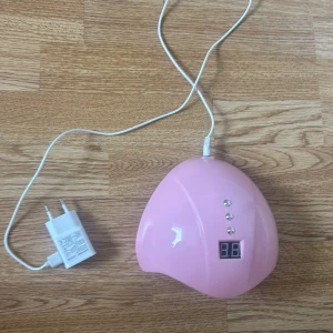 Rosa UV-lampa för naglar - Säljer en rosa UV-lampa för naglar med digital display och timerknappar för 30, 60 och 99 sekunder. Lampan har flera LED-lampor på insidan och kommer med vit laddare. Perfekt för gelnaglar hemma.