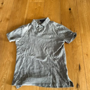 Grå pikétröja Polo Ralph Lauren M - Snygg grå pikétröja från Polo Ralph Lauren i slim fit. Klassisk krage med två knappar och broderad logga på bröstet. Tillverkad i mjuk bomull som är skön mot huden. Perfekt för dig som gillar stilren och enkel design.