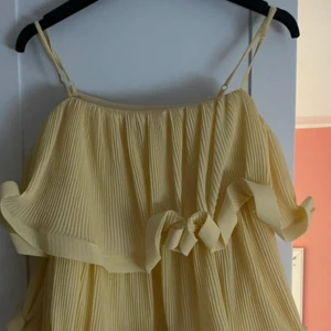 Gul plisserad volangblus NA-KD - Superfin gul blus från NA-KD med tunna axelband. Blusen har volangdetaljer framtill och är luftig med en flowy känsla, perfekt för varma dagar. Jag har den även ute på min Vinted för samma pris. Klänningen är aldrig använd och storlek 38