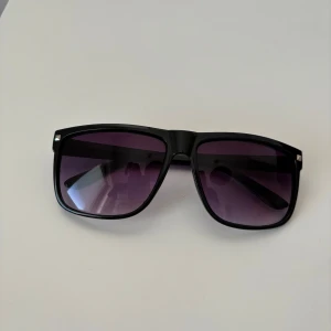 Raybans boyfriend liknande  - Snygga solglasögon med svart, fyrkantig båge och lila tonade glas. Klassisk modell med breda skalmar och diskreta silvriga detaljer vid hörnen. Perfekta för att lyfta din stil under soliga dagar. Helt nya