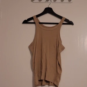 Beige linnetopp med breda axelband - Säljer en enkel och stilren beige linnetopp med breda axelband och rund halsringning. Toppen är ärmlös och har en avslappnad passform, perfekt för varma dagar. Materialet känns mjukt och lätt mot huden.