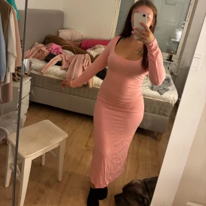 Ljusrosa långklänning med lång ärm - Säljer en superfin ljusrosa långklänning med lång ärm och rundad halsringning. Klänningen har en tight passform som framhäver figuren och är tillverkad i mjukt bomullsmaterial. Perfekt för dig som gillar enkel och stilren look med lite extra färg.