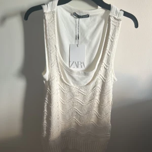 Vit stickad linnetopp från Zara - Supersöt vit linnetopp från Zara med stickad framsida i vågigt mönster och ribbad nederkant. Toppen har ett snyggt band på ryggen, perfekt att stayla med ett par jeans eller en kjol. Helt oanvänd (prislappen är på)