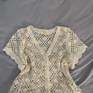 Vit virkad blus med knappar - Superfin vit virkad blus från Ribelle med korta ärmar och v-ringning. Blusen har stora dekorativa knappar framtill och ett snyggt hålmönster, den är köpt i usa och står att den är i storlek L men den passar på mig som brukar ha storlek Xs/S 🤍