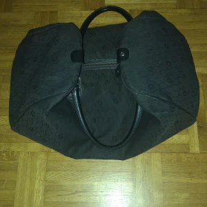 Svart weekendbag med mönster dior  - Stor svart weekendbag med diskret hexagonmönster och små loggor över hela väskan. Väskan har två rejäla handtag i skinn och dragkedja upptill. Perfekt för resor eller när du behöver extra plats.