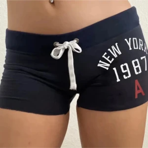 Svarta tighta shorts med snörning - Svarta, tighta shorts med vit snörning i midjan och tryck med texten 'New York 1987' framtill. Kommer ej till användning