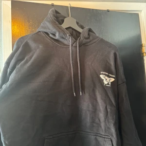 Svart hoodie med fjärilstryck yourturn - Svart hoodie från yourturn med coolt vitt tryck av fjärilar och växter på ryggen samt mindre tryck på bröstet. Tröjan har huva med snörning och stor känguruficka framtill. Perfekt för dig som gillar unika prints och streetwear vibes.