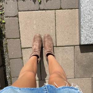 Bruna mockaboots med kilklack - Snygga bruna boots i mocka med kilklack och rund tå. Skorna har en enkel och stilren design med diskreta sömmar och en liten flik upptill. Perfekta för dig som vill ha en trendig och bekväm look till hösten.