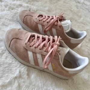 Adidas Gazelle rosa sneakers mocka - Snygga Adidas Gazelle sneakers i ljusrosa mocka med vita detaljer och klassiska tre ränder på sidorna. Fläckar förekommer men tror man kan fräscha upp dom enkelt med skotvätt. Inte mycket använda så sulan är inte sliten. 