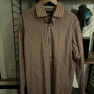 Rutig skjorta från Hugo Boss, strl 44 - Snygg rutig skjorta från Hugo Boss i regular fit. Skjortan har ett klassiskt rutmönster i orange, blått och vitt, lång ärm och knappar framtill. Perfekt för dig som gillar stilrena och färgglada plagg med en modern touch.