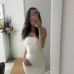 Vit klänning - Säljer en vit, figurnära och kortklänning med snyggt rynkad design från Nelly. Klänningen har en rak halsringning och sitter slim på kroppen för en riktigt clean och modern look. Perfekt för dig som gillar minimalistisk stil och vill sticka ut. I storlek storlek 36/S