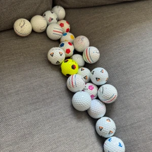 Coola bollar 5 st fotbollar och 3 st tp5 pix - Bilden visar ett antal golfbollar i olika färger och mönster, placerade på en grå soffa. Ingen bok syns på bilden.