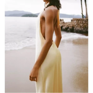 Gul långklänning i satin - Säljer en elegant gul långklänning i satin med halterneck och öppen rygg. Klänningen har en snygg knytning i nacken och ett mjukt, flytande fall som ger en lyxig känsla. Perfekt för dig som vill sticka ut med en stilren och sofistikerad look.