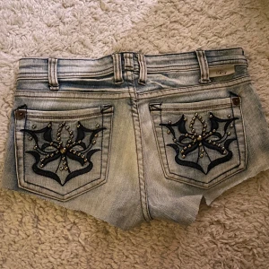 Fishbone jeansshorts med nitar - Snygga ljusblå jeansshorts från Fishbone med rå kant och slitningar. Framtill finns coola nitar vid fickorna och baktill är fickorna dekorerade med svart broderi och nitar i ett mönster. Skriv för frågor!
