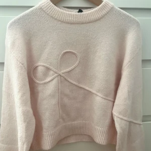 Ljusrosa stickad tröja med rosettdetalj - Supersöt ljusrosa stickad tröja med en rosettdetalj framtill. Den är helt och hållet oanvänd och är då i jättebra skick. Hör av er om ni har några frågor😊