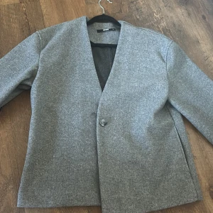 Grå kappa från BikBok XS - Stilren grå kappa från BikBok i storlek XS. Jackan har en enkel knäppning med en knapp framtill, rak passform och lång ärm. Perfekt för dig som gillar minimalistisk look och vill ha något som funkar till många outfits.