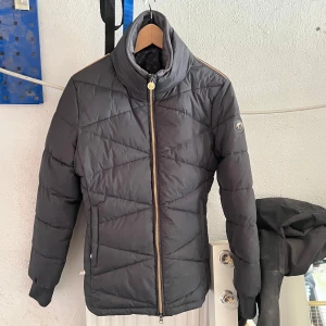 jacka från Covalliero - Snygg jacka från Covalliero med guldfärgad dragkedja och hög krage. Jackan har quiltad design, långa ärmar och två fickor framtill. Perfekt för kalla dagar när du vill hålla stilen och värmen.