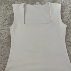 Vit linnetopp med fyrkantig hals - Snygg vit linnetopp från Gina Tricot med fyrkantig halsringning och ärmlös design. Toppen har en clean och stilren look, perfekt att matcha med jeans eller kjol. Materialet känns mjukt och har en lätt stretch för skön passform. Har typ använt 1-2 gånger 