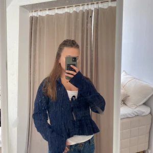 Mörkblå stickad kofta från Nelly - Supersöt mörkblå stickad kofta från Nelly med knyt framtill. Koftan har lång ärm och en lätt volangkant nedtill som ger en extra touch. Perfekt att slänga över ett linne eller t-shirt för en chill look.