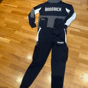Mörkblå och grå hoodie från Hoodrich - Snygg hoodie från Hoodrich i mörkblått , grått och vitt med stor logga på bröstet och ärmen. Tröjan har huva och långa ärmar, samt ribbade muddar. Perfekt för en streetwear-look och riktigt skön att bära. Kommer med byxor.