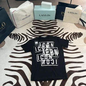 Svart Dsquared2 ICON t-shirt M - Svart t-shirt från Dsquared2 med stor vit grafisk print där det står 'ICON' i flera lager på framsidan. Klassisk rund hals och korta ärmar. Snygg och modern design som sticker ut. Materialet är mjuk bomull som känns skönt mot huden.